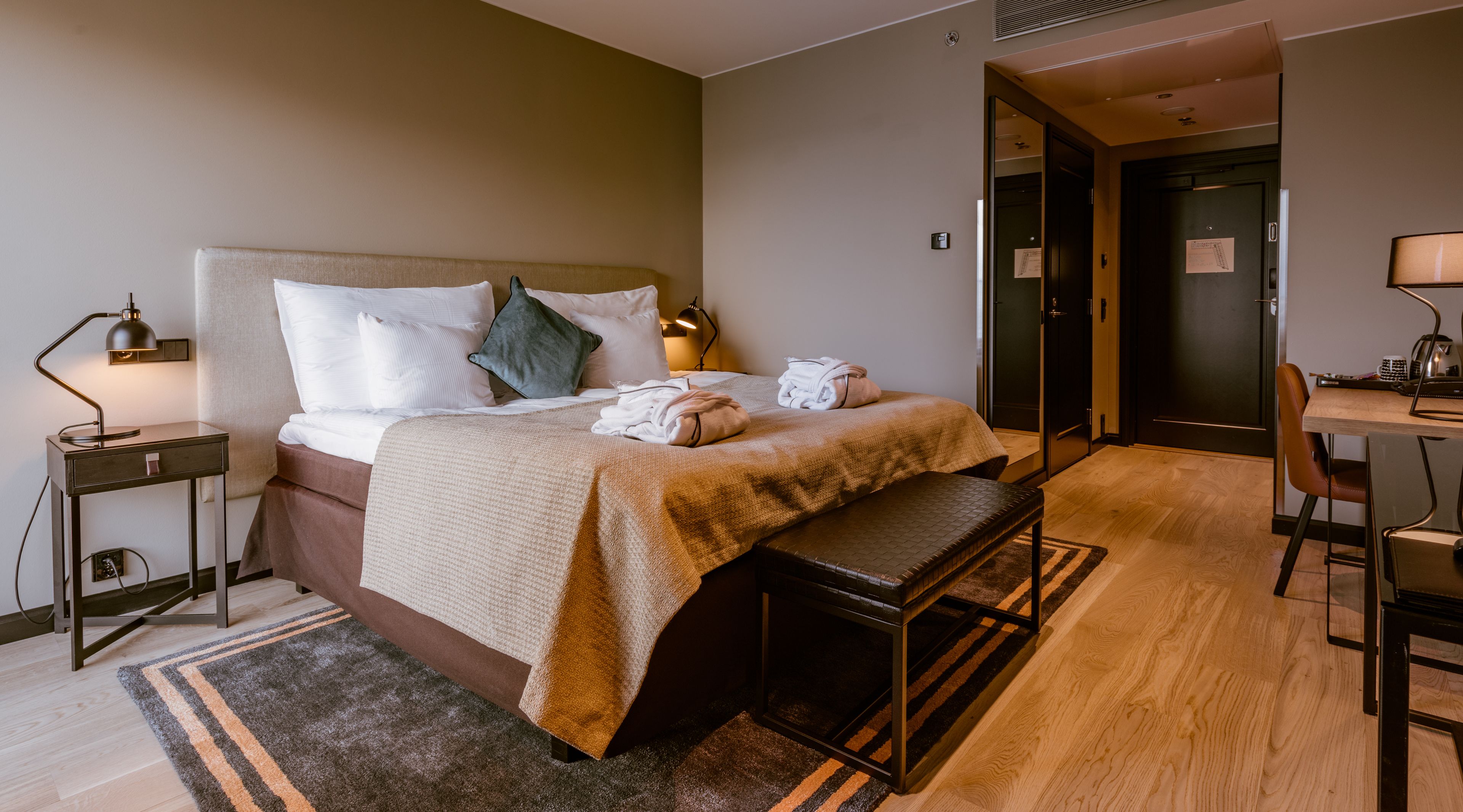 A hotel room with a bed, bedside tables, a desk, and a chair.