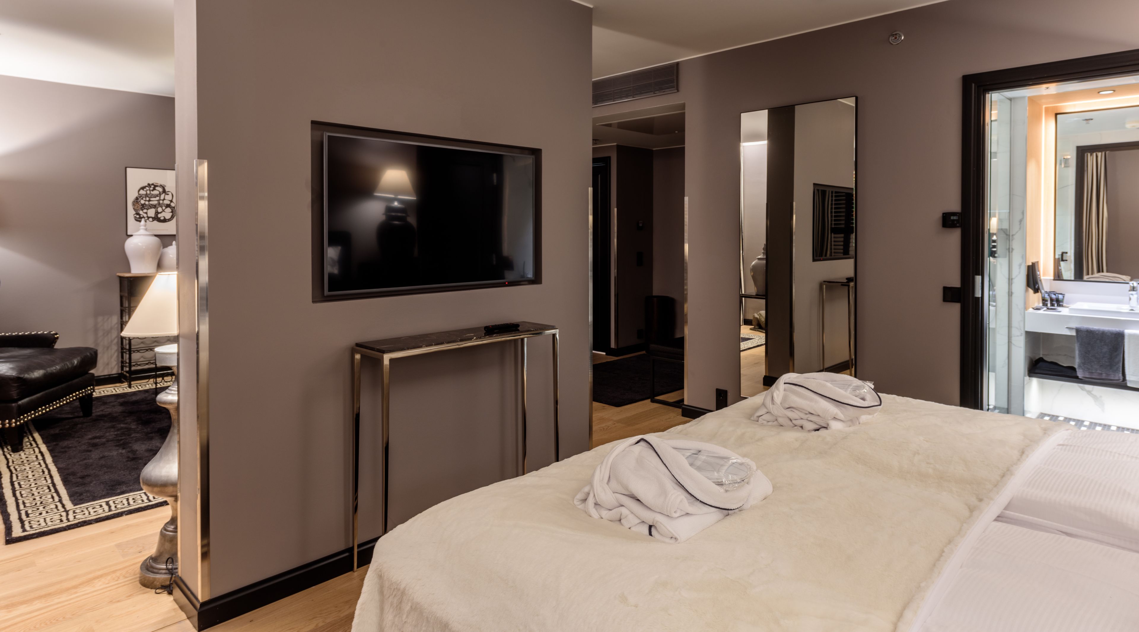 A hotel room with a bed, a TV, a desk, and a bathroom visible through an open door.