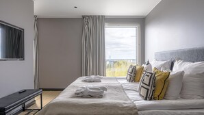 Una habitación de hotel moderna con una cama grande, una mesita de noche, un televisor y una ventana con cortinas.