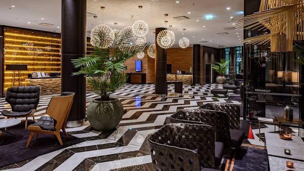 Un vestíbulo moderno con un mostrador de recepción, zonas de estar y una gran planta decorativa.