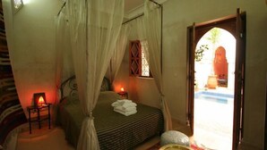 Un dormitorio con cama con dosel, una mesita de noche con lámpara y vistas a un espacio exterior.