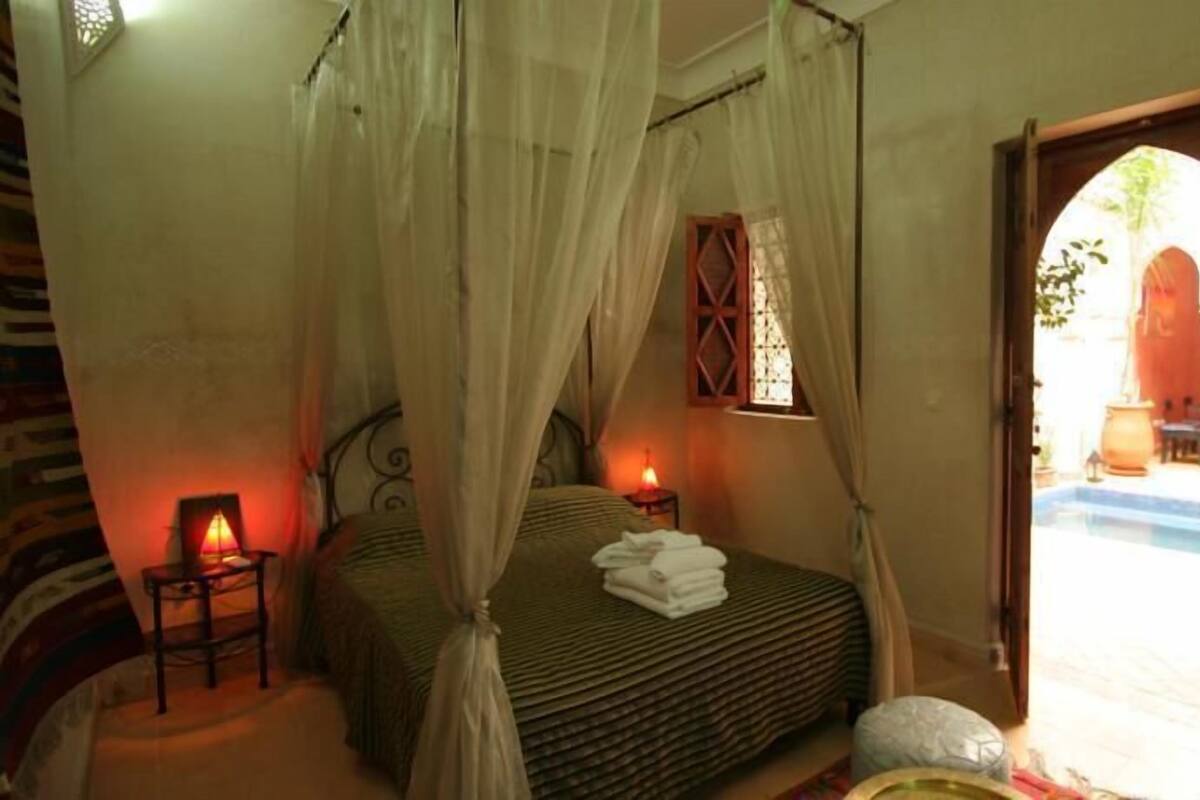 Quarto com cama de dossel, mesa de cabeceira com abajur e vista para área externa.