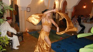 Una mujer con un vestido dorado actuando en una sala con arcos y una alfombra azul.