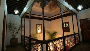 Estructura de madera tradicional con barandilla decorativa, una planta en maceta y una ventana iluminada, que sugiere un espacio interior tranquilo.