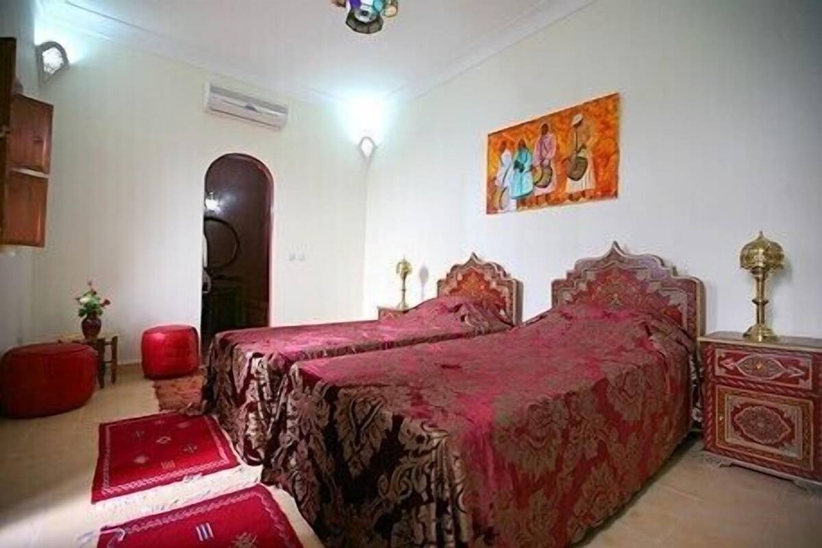 Quarto com duas camas, porta de madeira, um quadro e uma mesinha com abajur.