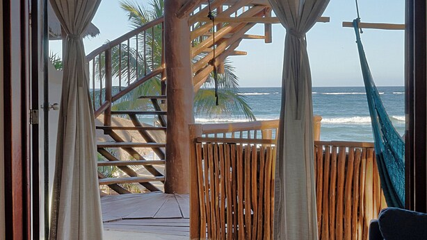A bedroom with a view of the ocean, a hammock, and a wooden staircase leading to a balcony. - Playa Canek Beachfront Eco Hotel (Tulum)