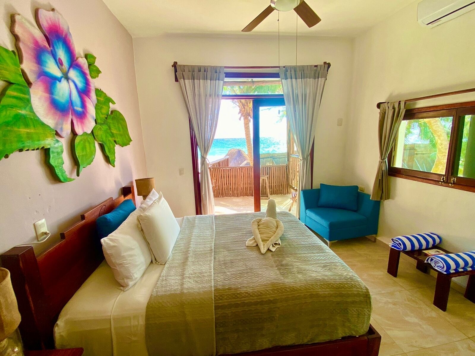 Un dormitorio con cama, ventilador de techo, vista al océano y balcón con valla de madera.