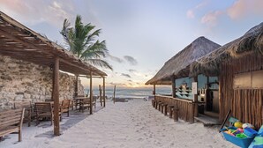 A beachside restaurant with wooden benches and tables, a thatched-roof building, and a view of the ocean. - Playa Canek Beachfront Eco Hotel (Tulum)
