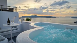 Un jacuzzi con vistas al mar y a las montañas, una mesa con una botella y vasos, y mobiliario blanco para exteriores.