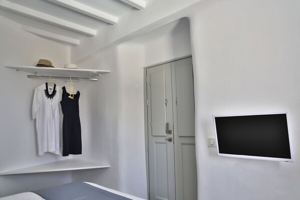 Un dormitorio con cama, armario, televisor montado en la pared y estante con ropa y un sombrero.
