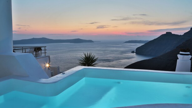 Una piscina infinita moderna con vista al mar y a islas lejanas al atardecer.