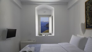 Un dormitorio con cama, ventana con vista al mar, televisión de pantalla plana y mesita de noche.