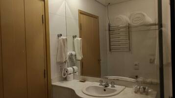 Un baño con lavamanos, espejo, toallero y dispensador de toallas.