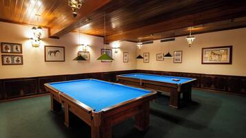 Sala com mesa de bilhar, duas mesas de bilhar, teto de madeira e quadros nas paredes.