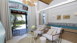 Una sala de estar moderna con un sofá, sillones, una mesa de centro de cristal y vistas a un jardín.