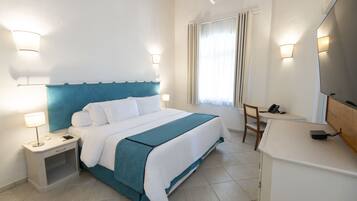 A hotel room with a bed, bedside table, lamp, chair, desk, and a mirror.