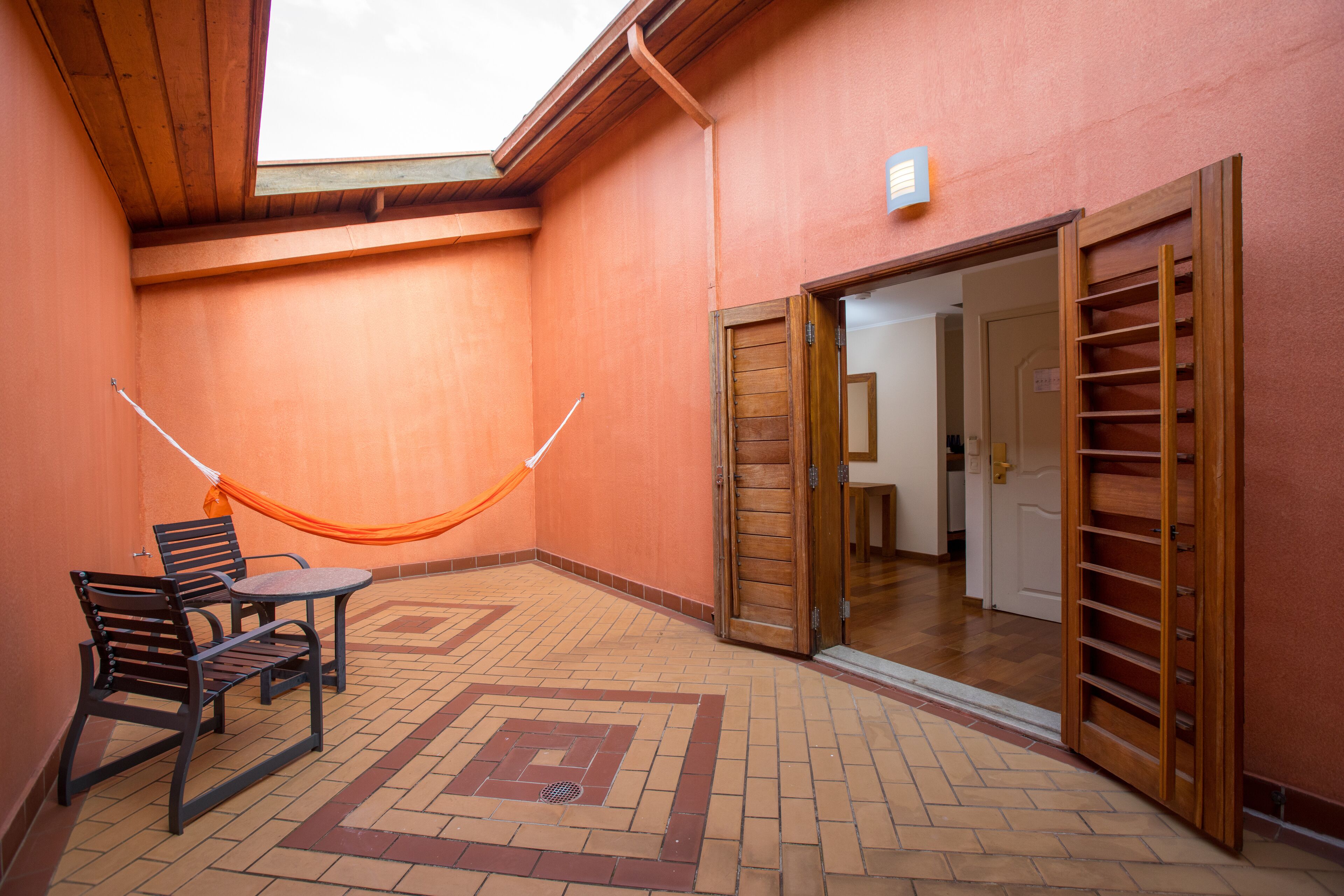 An outdoor patio area with a wooden table and chairs, a hammock, and a sliding door leading to an interior space.