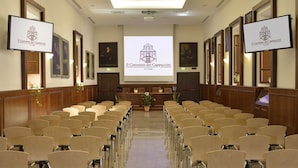 A conference room with rows of chairs facing a screen displaying 'Il Convento dei Cappuccini'. - Casa I Cappuccini (Rome)