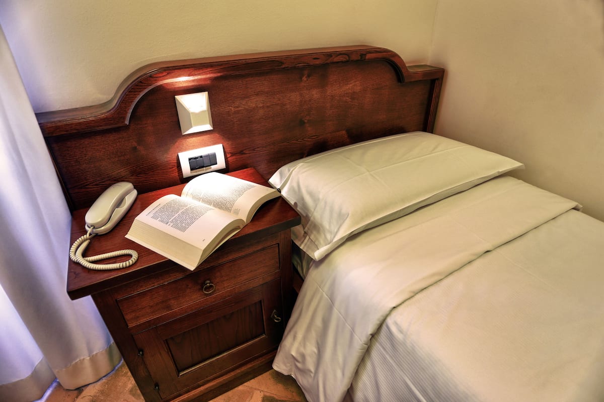 A wooden bedside table with a telephone, an open book, and a bedside lamp.