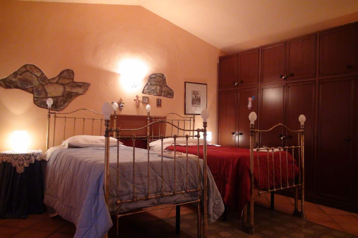 A bedroom with two beds, a stone wall decoration, a cross, and a framed picture.