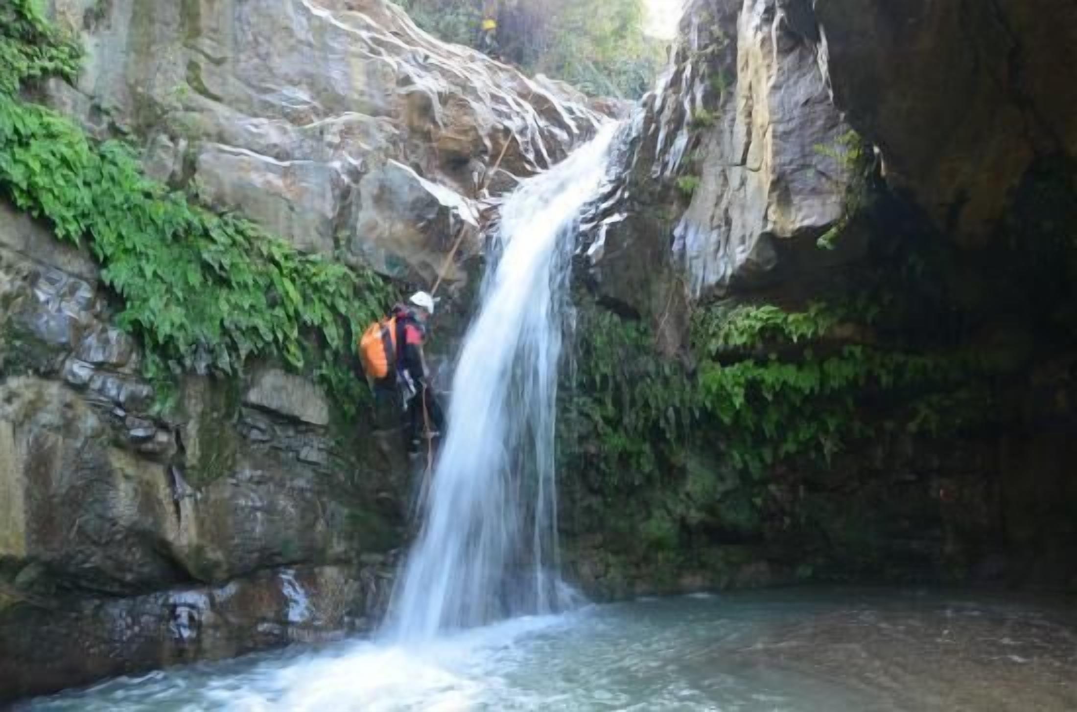 Una cascada en un desfiladero rocoso con una persona escalando las rocas.