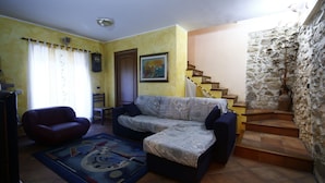 A living room with a sofa, a chair, a rug, a painting, a clock, and a staircase with stone walls. - Heart of Sicily (Mistretta)