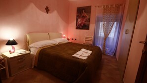 A bedroom with a bed, bedside table with a lamp, a cross on the wall, and a painting. - Heart of Sicily (Mistretta)