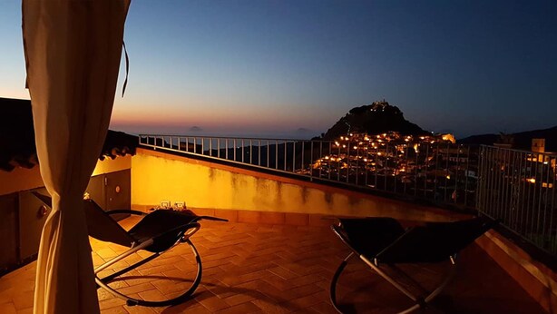 A balcony with a view of a town at dusk, featuring a railing and two chairs. - Heart of Sicily (Mistretta)