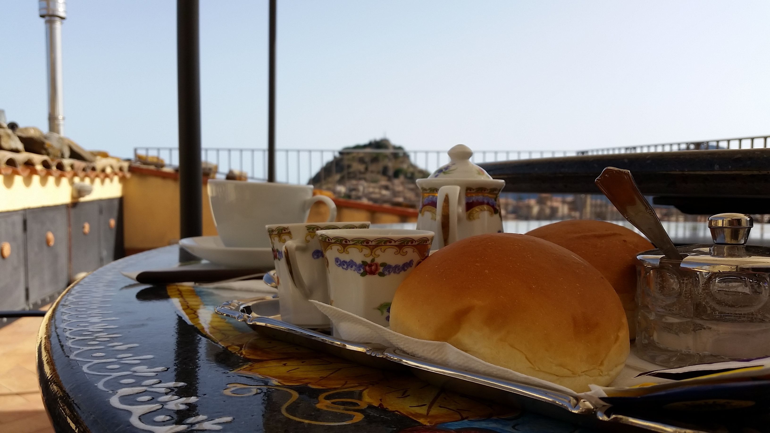 A table with a tray containing two rolls of bread, a teapot, a cup, and a sugar container.