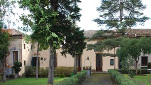 A traditional building with a tiled roof, a central entrance, and a well-maintained garden with hedges and trees. - Case Zuccaro (Trecastagni)