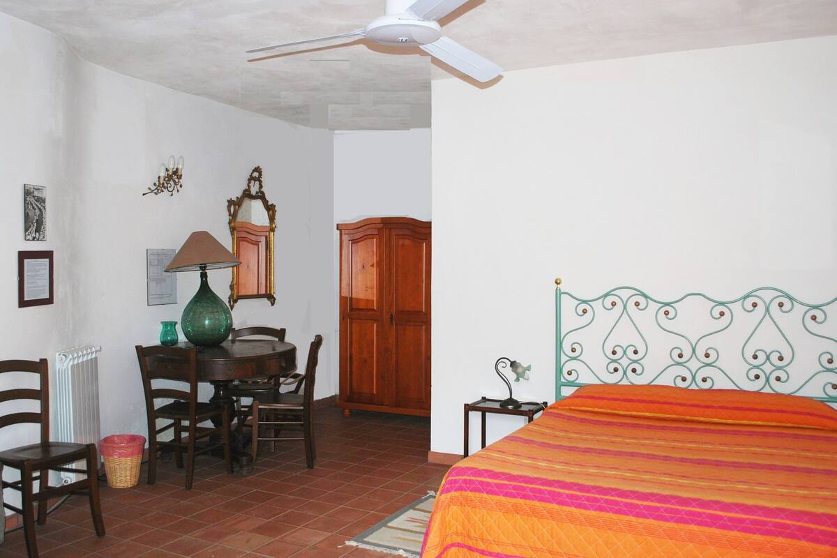 Un dormitorio con una cama, un escritorio con lámpara, una silla, un armario de madera y un radiador.
