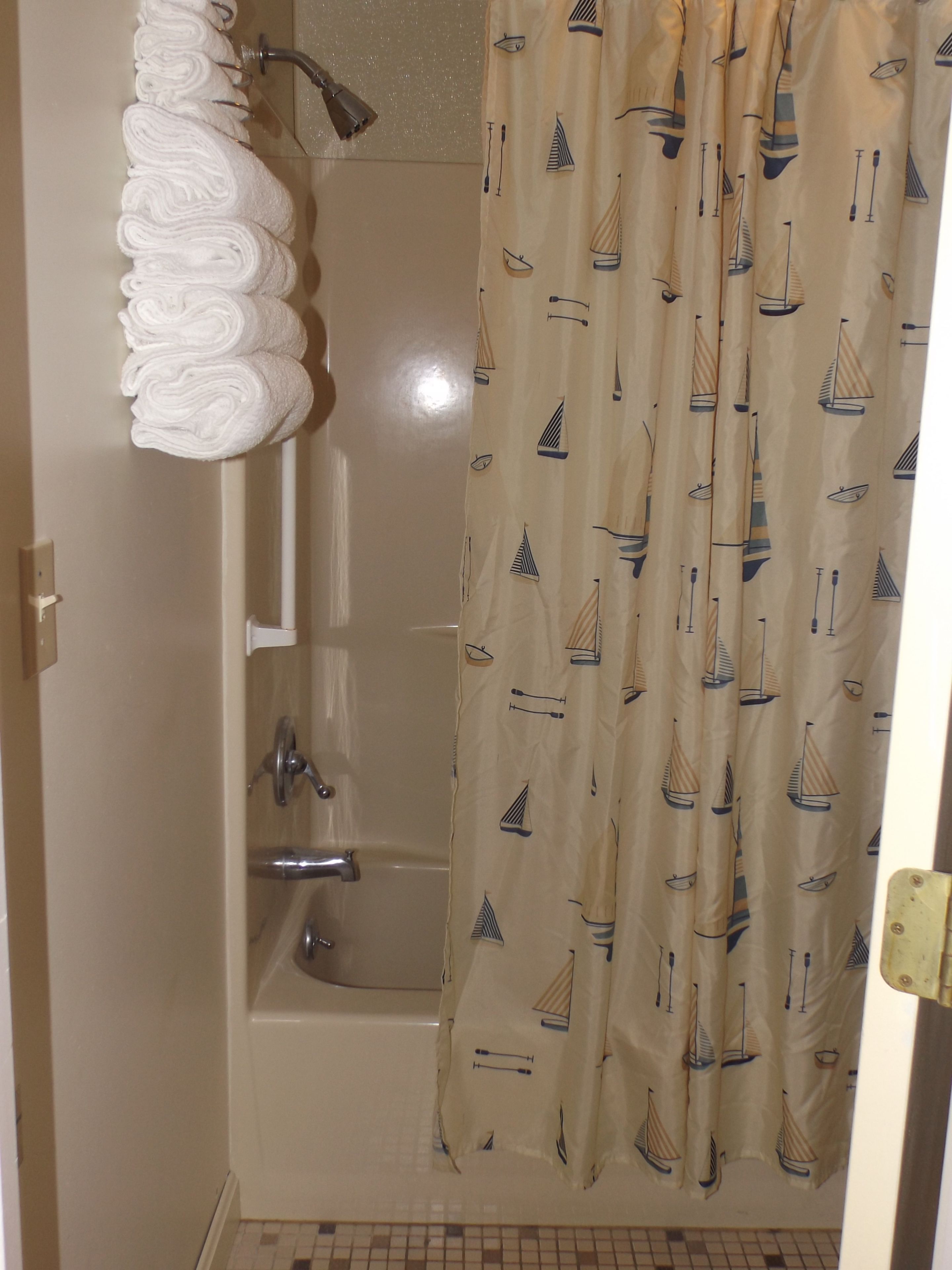 A bathroom with a bathtub, a shower, and a towel rack with neatly rolled towels.