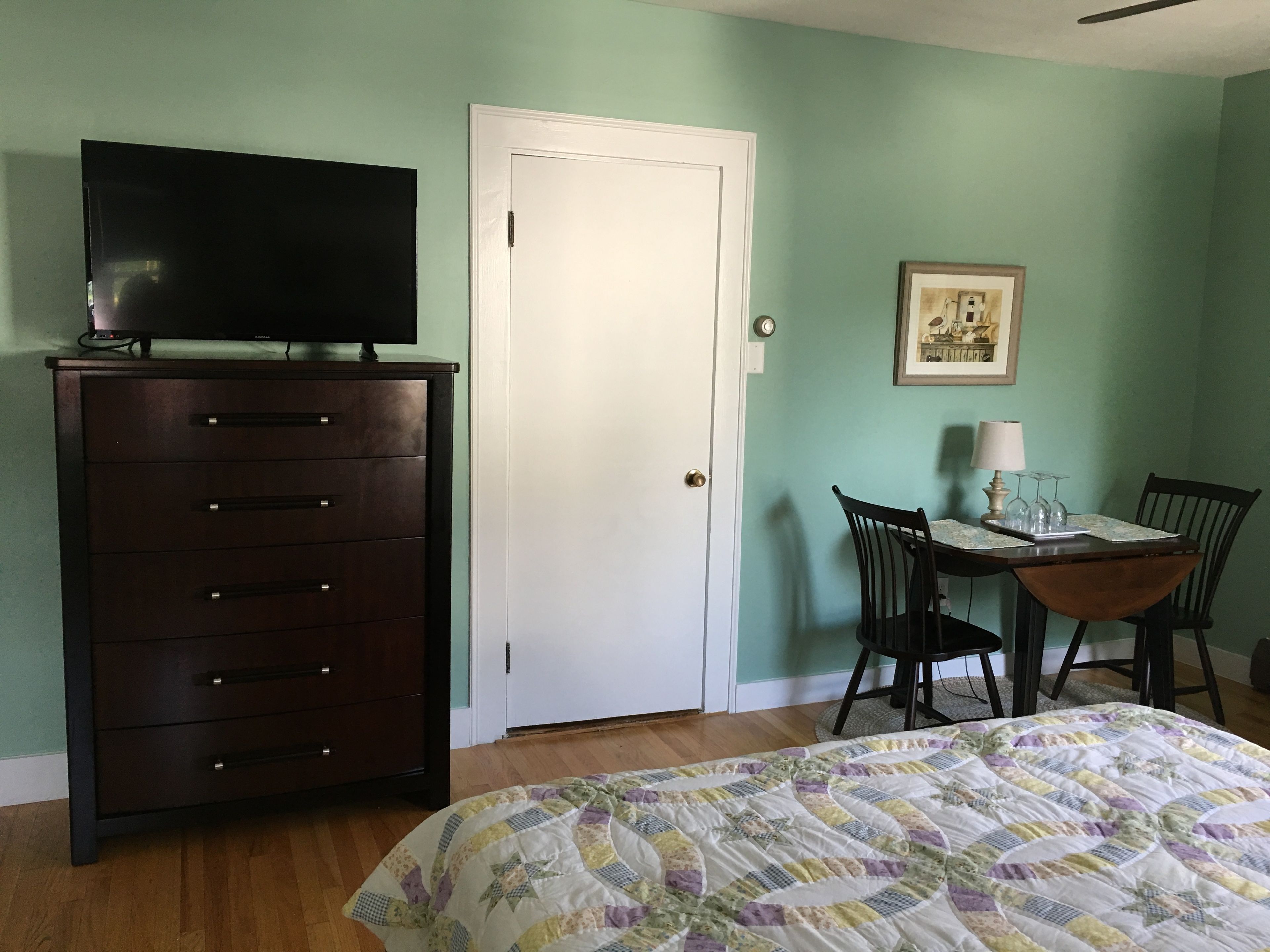 A bedroom with a bed, dresser, television, and a dining table with chairs.