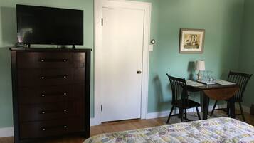 A bedroom with a bed, dresser, television, and a dining table with chairs.