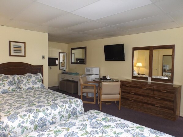 Habitación de hotel con dos camas, un escritorio, una silla, un televisor y un aparador.