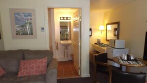 Una camera d'albergo con divano, angolo ristoro con tavolo e sedie, angolo cottura e bagno con lavandino e specchio.