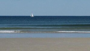 Una spiaggia con una barca a vela all'orizzonte.