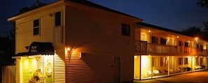 Un hotel con recepción, un balcón con mobiliario exterior y una entrada bien iluminada.