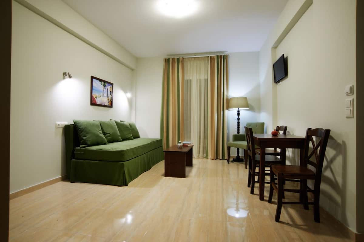 A small, well-lit room with a green sofa, a small table, and a dining area with chairs.
