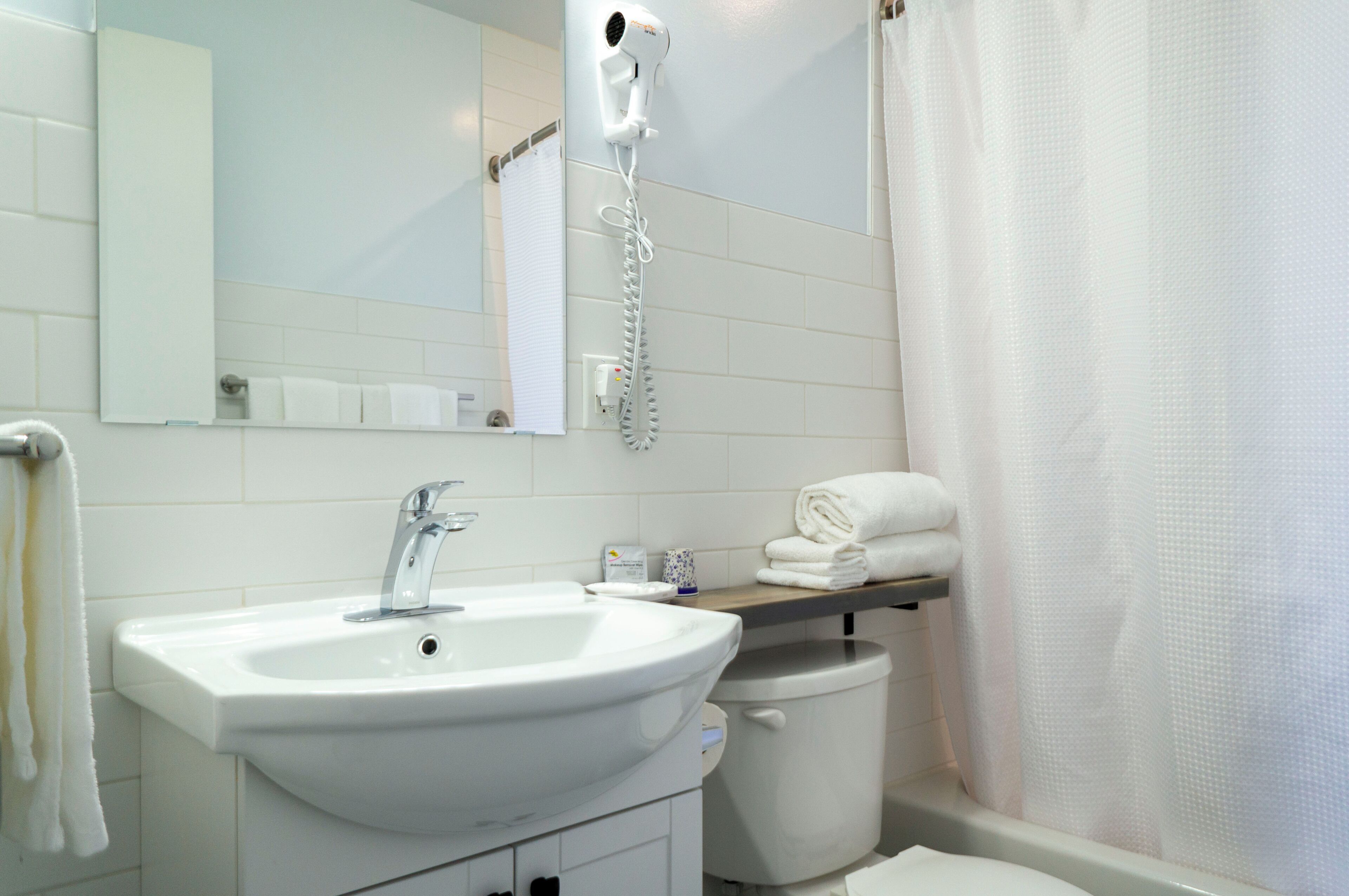 Een badkamer met een witte wastafel, een spiegel, een haardroger, een handdoekhouder en een douchegordijn.