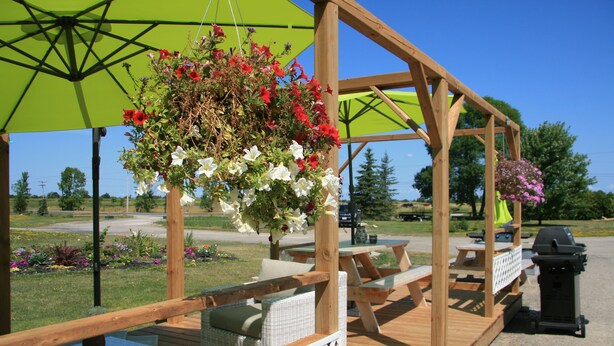 A wooden deck with outdoor seating, a hanging flower basket, and a barbecue grill. - Wayside Motel Manitoulin (Assiginack)