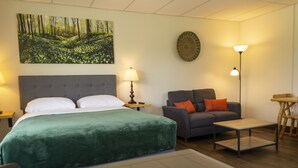 A hotel room with a large bed, a grey sofa, a small table, and a lamp. - Wayside Motel Manitoulin (Assiginack)