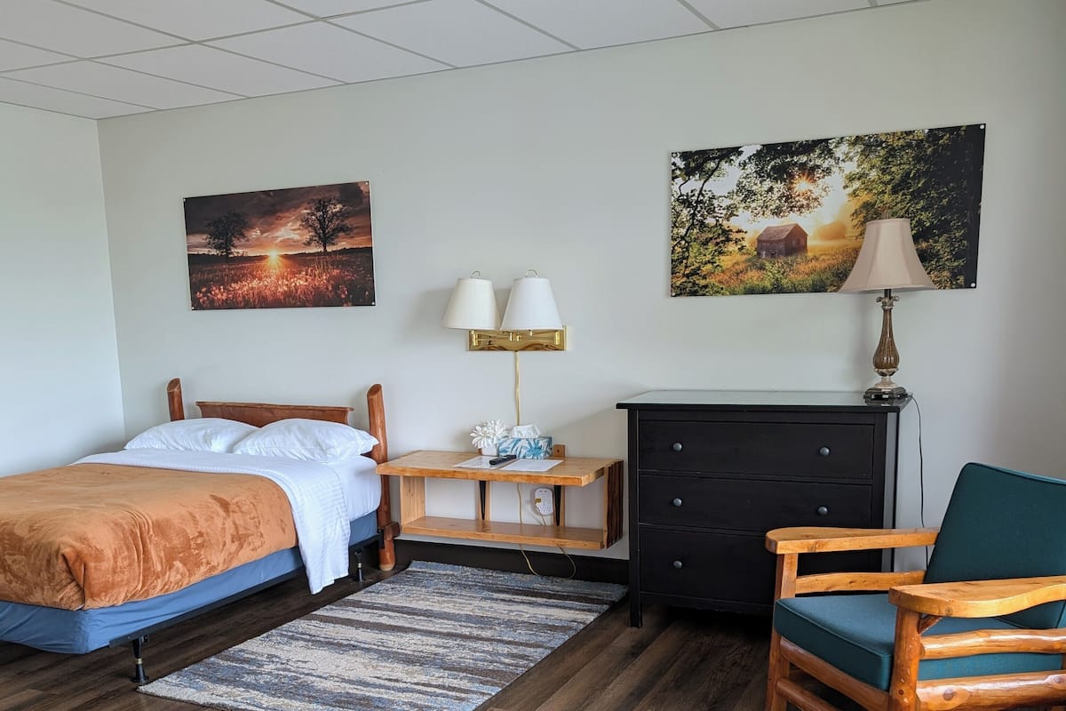 A hotel room with a bed, a desk, a dresser, a chair, and two wall-mounted lamps.