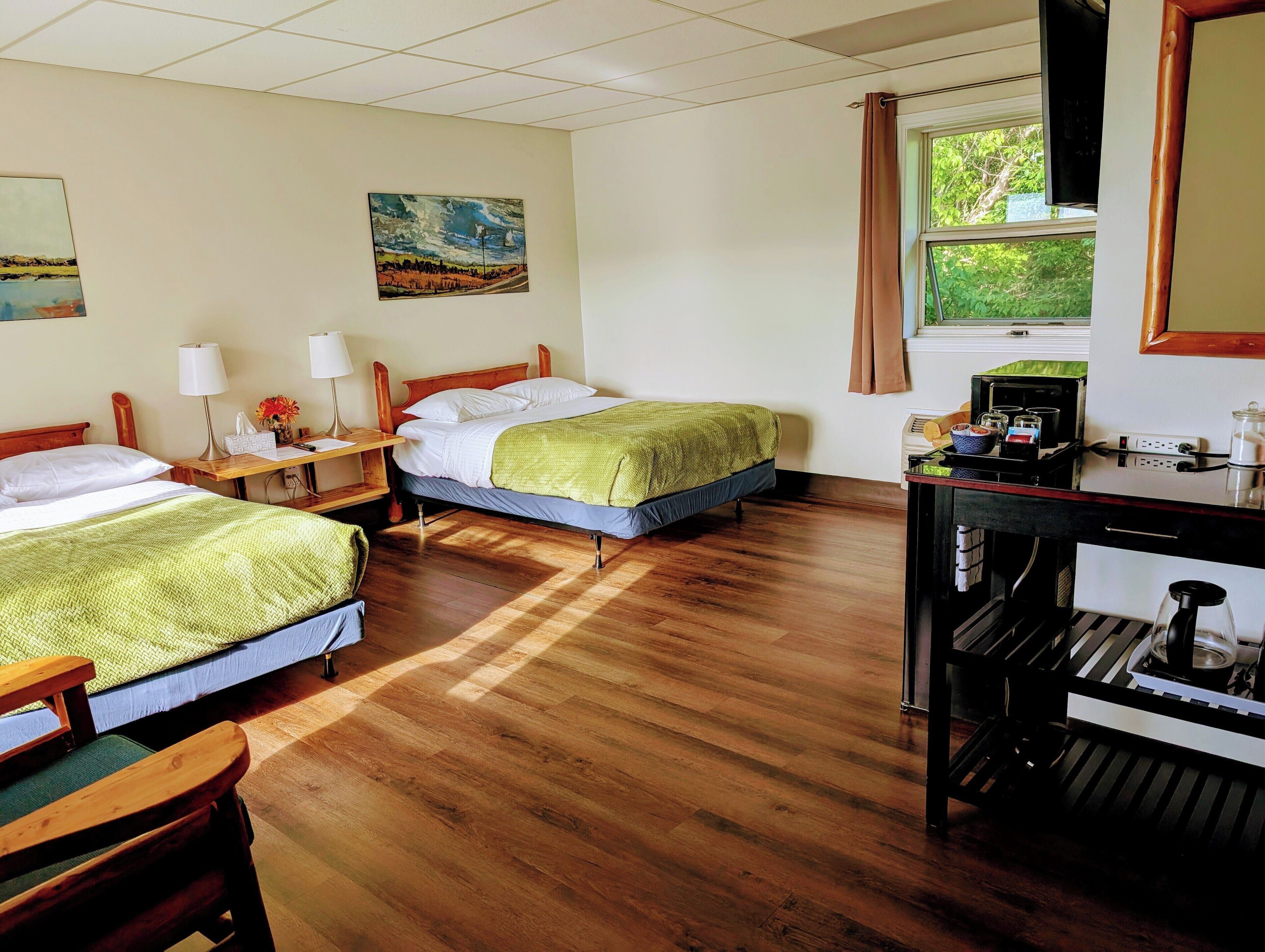 A hotel room with two beds, wooden flooring, a desk with a coffee machine, and artwork on the walls.