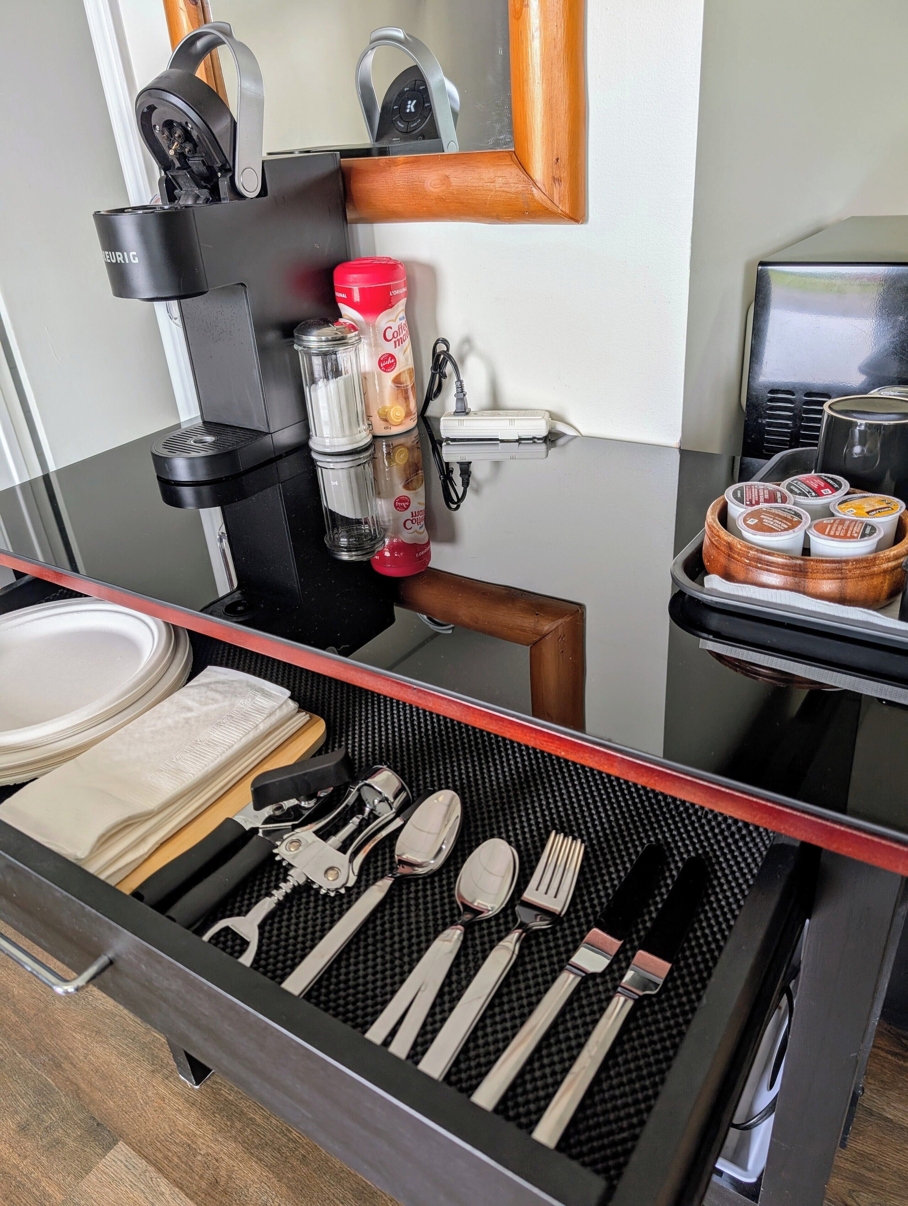Morgenmadsområde på et hotelværelse med kaffemaskine, kaffekapsler, en rød vandflaske og en bakke med morgenmadsprodukter.