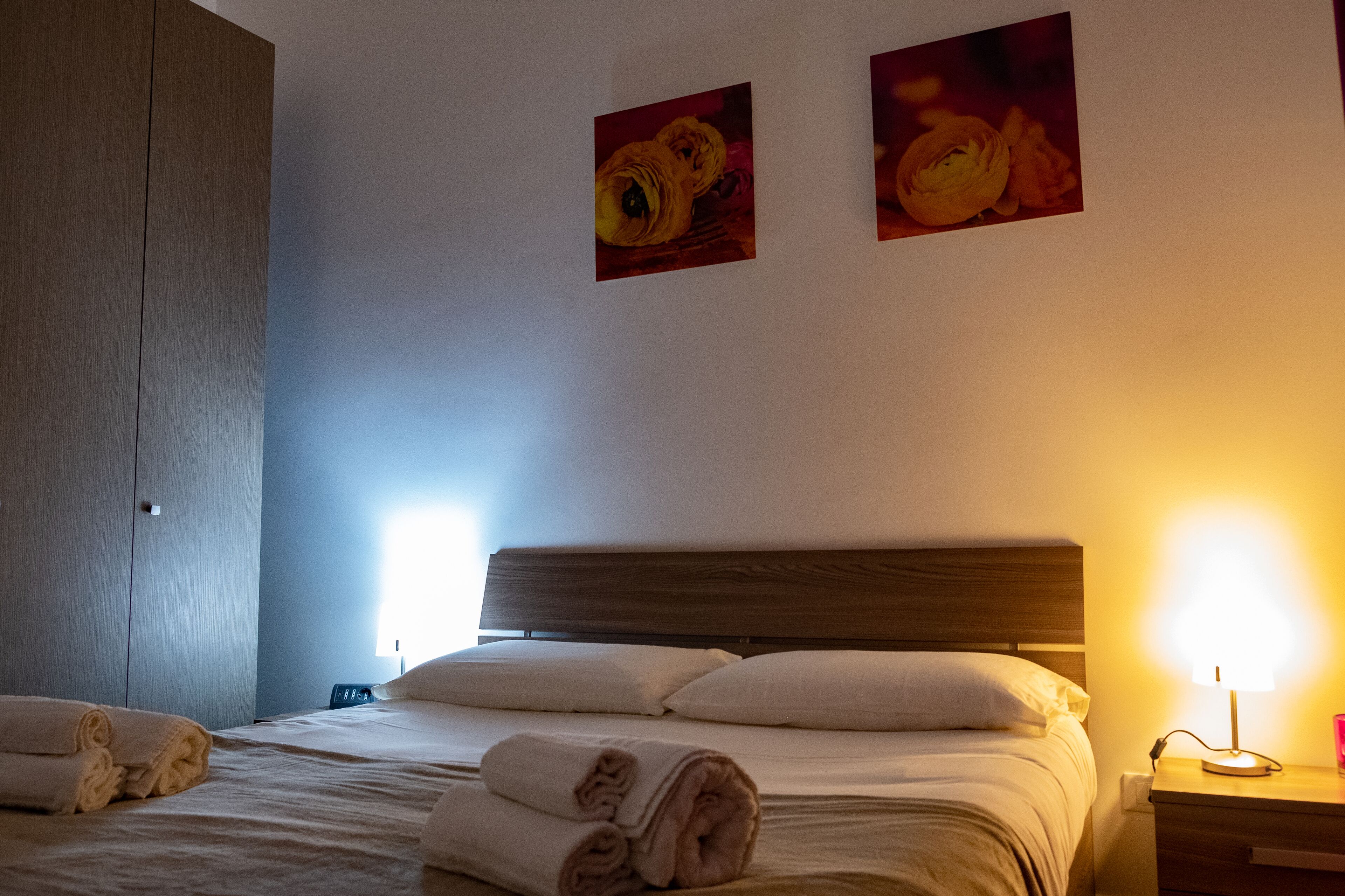 A hotel room with a bed, two wall-mounted lamps, and a wardrobe.