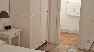 Un dormitorio con cama, armario, mesita de noche con lámpara y baño visible a través de una puerta abierta.