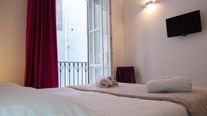 A hotel room with two beds, a TV mounted on the wall, and a balcony with a red curtain. - B&B Teatro (Palermo)