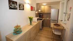 A compact kitchen with wooden cabinets, a microwave, a stove, and a refrigerator. There are wall-mounted lights, a small dining table with chairs, and a tray of food on the counter. - B&B Teatro (Palermo)