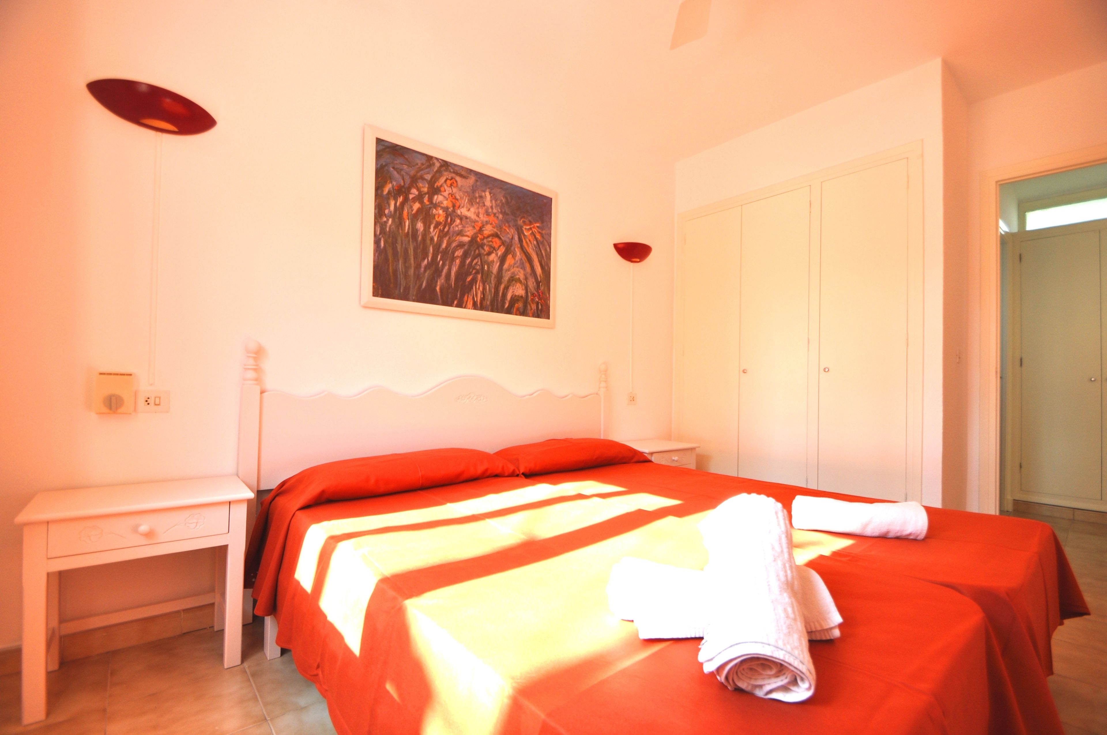 Een slaapkamer met een bed, nachtkastje, schilderij aan de muur en een kledingkast.
